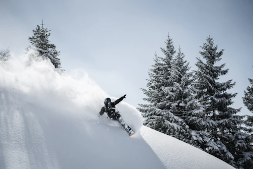 A skier carving fresh powder on a steep alpine slope under clear blue skies.
