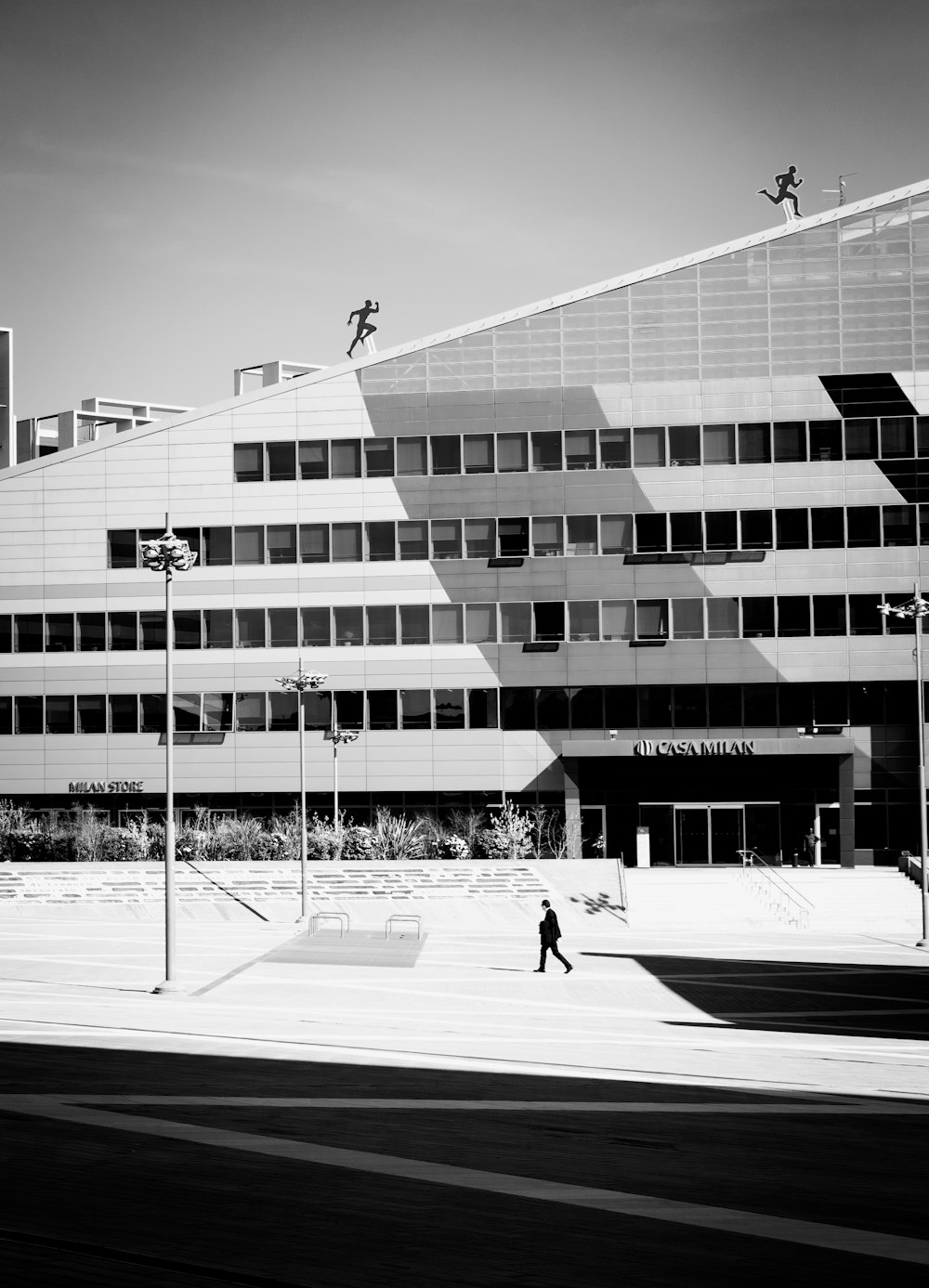 a black and white photo of a person walking in front of a building