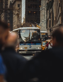 A sleek charter bus parked in front of a bustling NYC skyline at sunset.