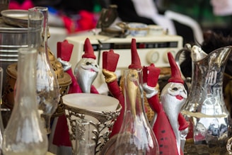 A collection of vintage and decorative items are displayed, including several Santa Claus figurines holding candles, various ornate glass and metal objects, and an old radio in the background.