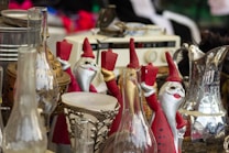 A collection of vintage and decorative items are displayed, including several Santa Claus figurines holding candles, various ornate glass and metal objects, and an old radio in the background.
