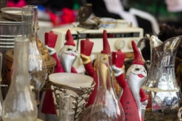 A collection of vintage and decorative items are displayed, including several Santa Claus figurines holding candles, various ornate glass and metal objects, and an old radio in the background.