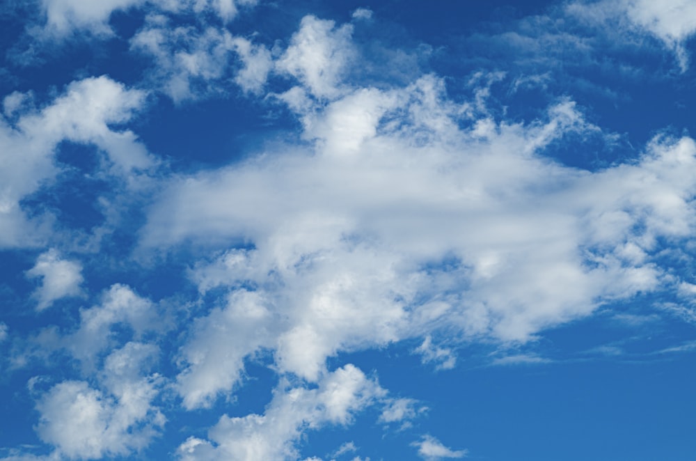 a plane flying through a blue sky with white clouds