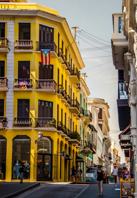 A lively street scene in Old San Juan with colorful buildings, palm trees, and locals enjoying a sunny day.
