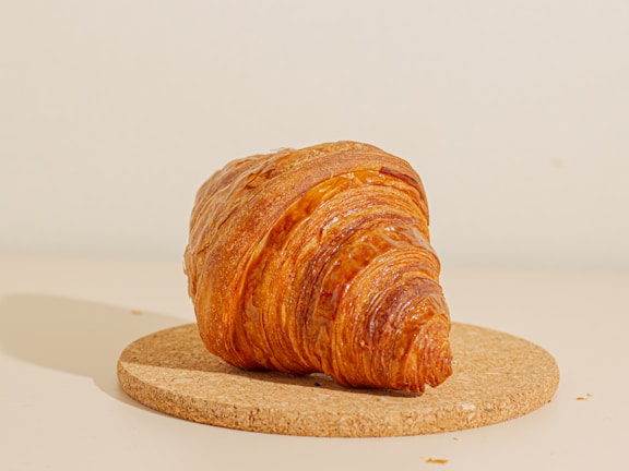 Close-up of a golden croissant resting on a rustic wooden table bathed in warm morning light.