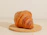 Close-up of a golden, flaky croissant resting on a rustic wooden table with soft morning light.