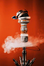 Close-up of a sleek black and gold hookah with swirling aromatic smoke against a dark charcoal background.