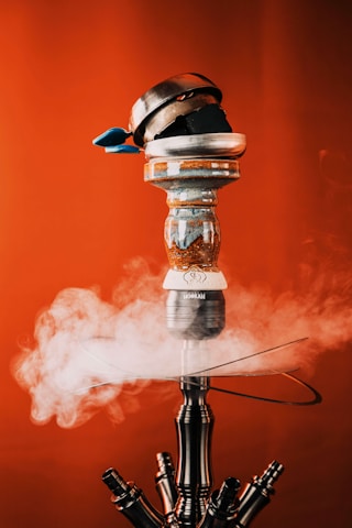 Close-up of swirling thick shisha smoke drifting above a luxury hookah with violet LED accents.