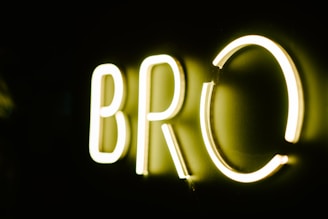 Brightly illuminated letters 'BRO' in neon lights against a dark background, casting a soft glow.