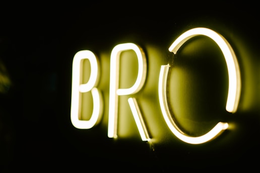Brightly illuminated letters 'BRO' in neon lights against a dark background, casting a soft glow.