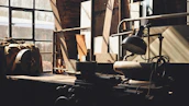 Industrial workshop scene with metal tools hanging against a concrete wall, lit by warm overhead lights.