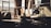 A dimly lit industrial workshop with a large window allowing beams of natural light to filter through. The room contains various machinery and tools, including a lathe, a lamp, and storage shelves. The setting appears aged and used, with dust and signs of wear on surfaces.