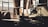 A dimly lit industrial workshop with a large window allowing beams of natural light to filter through. The room contains various machinery and tools, including a lathe, a lamp, and storage shelves. The setting appears aged and used, with dust and signs of wear on surfaces.