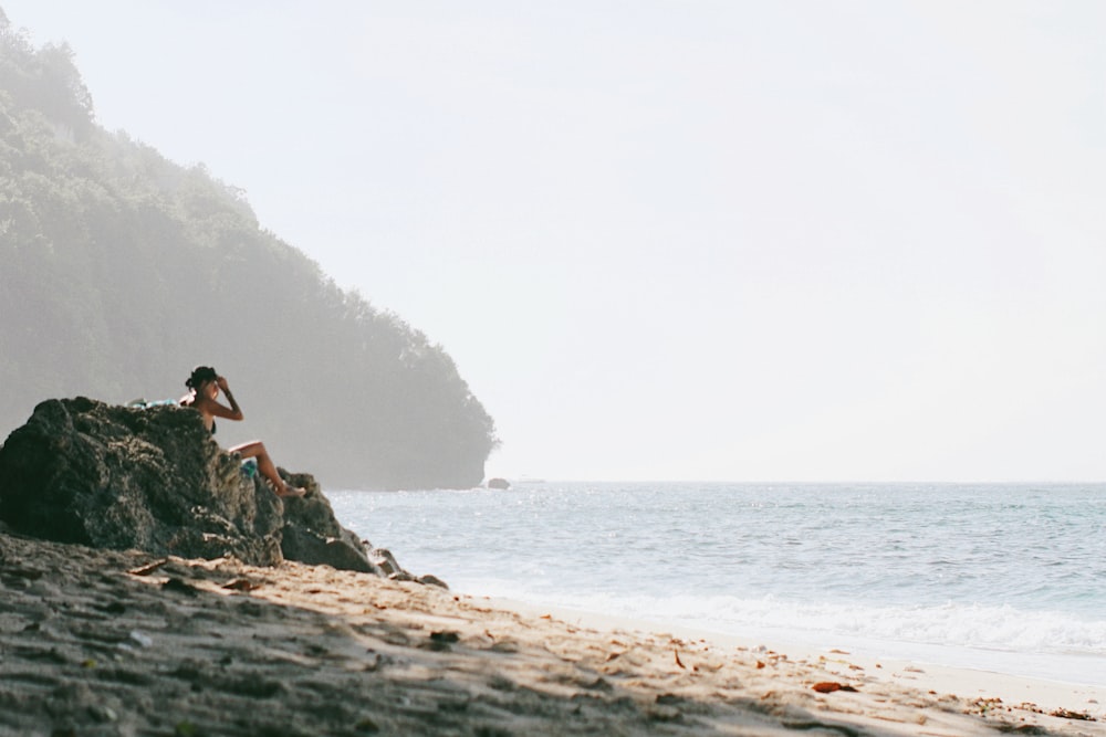 uma pessoa sentada em uma rocha na praia