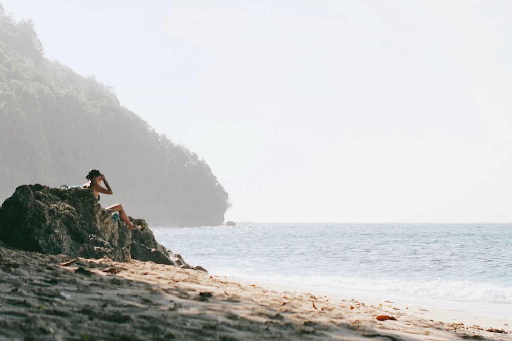 a person sitting on a rock on the beach