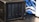 A black network-attached storage (NAS) device with four drive bays is placed on a black table. Blue and white cables are visible in the background.