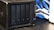 A black network-attached storage (NAS) device with four drive bays is placed on a black table. Blue and white cables are visible in the background.