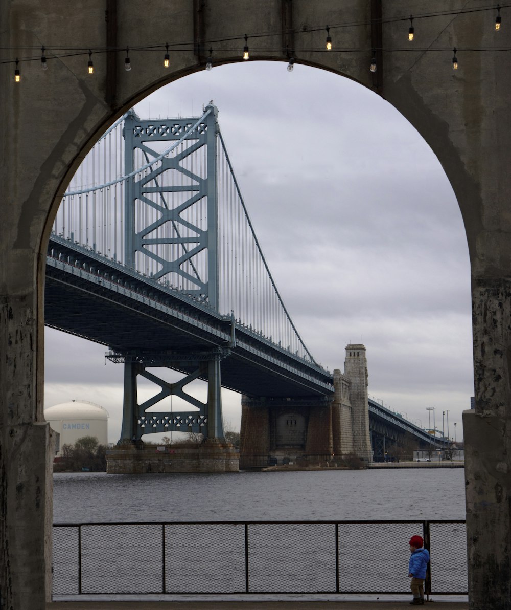 a person standing under a bridge looking at the water
