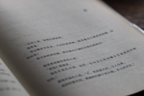 A close-up view of a book page with Chinese text in black ink. The page is slightly curved, indicating that the book is open. The lighting is soft and creates subtle shadows on the page, giving it a natural and somewhat intimate feel. The background is out of focus, emphasizing the text on the page.
