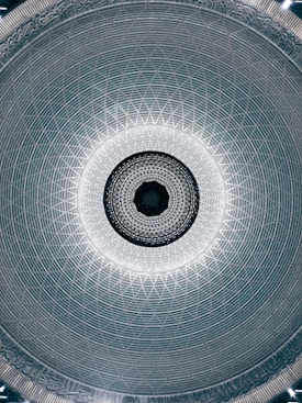 The image features a highly intricate and symmetrical dome with an ornate, geometric pattern. The central circular point is surrounded by concentric layers of lattice work, gradually expanding outward. The edge of the dome is decorated with detailed inscriptions and intricate designs.