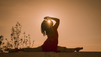 a woman sitting on a wall with the sun behind her