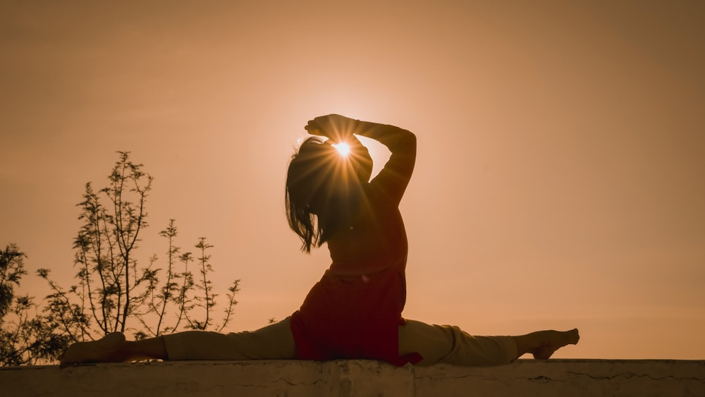 a woman sitting on a wall with the sun behind her