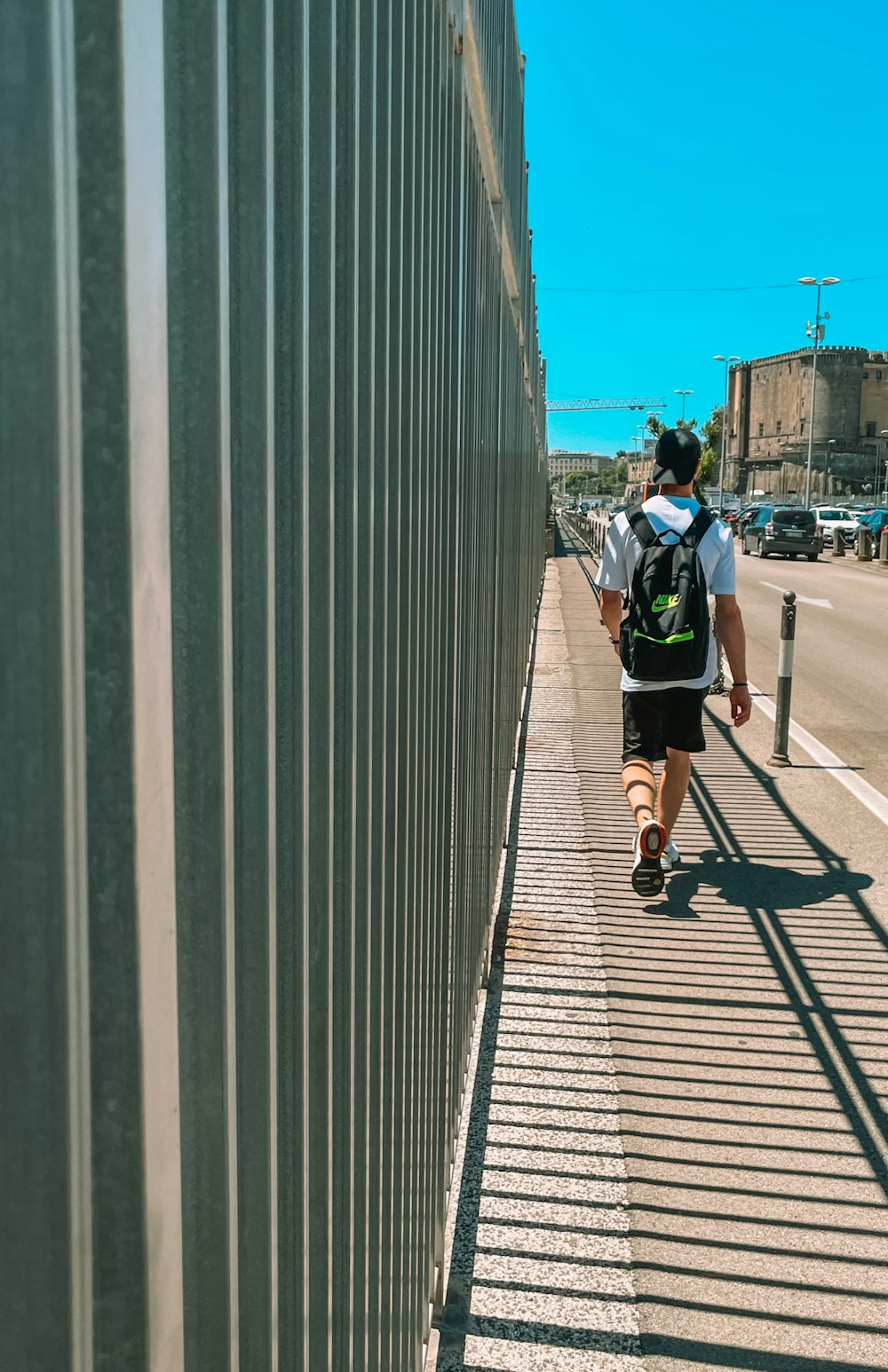 a man walking down a sidewalk next to a fence