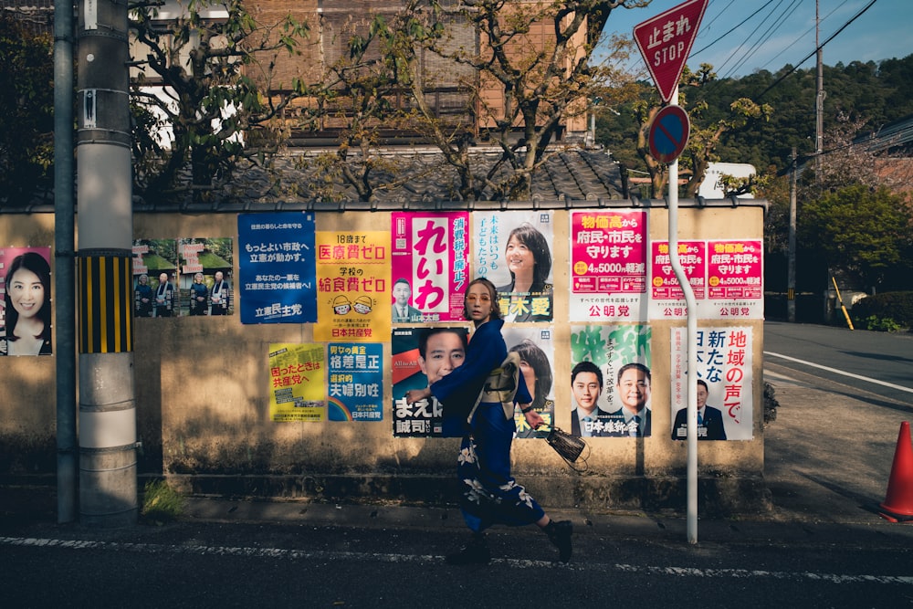 a man walking down a street past a wall covered in posters