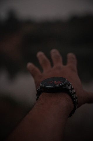 A hand reaching out with a dark wristwatch visible on the wrist. The background is blurred, giving a sense of depth and focus on the hand.