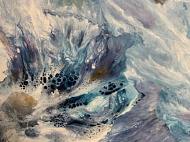 A dynamic abstract painting featuring swirling patterns of blue, white, and black with textured areas. The composition includes fluid lines and intricate cellular formations resembling ocean waves or cosmic elements.