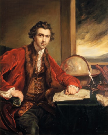 A man wearing a richly textured red coat with fur trim sits confidently at a desk. His hand rests on papers, and next to him is a large globe. The background includes a window with a dramatic, cloudy sky and stacks of books.