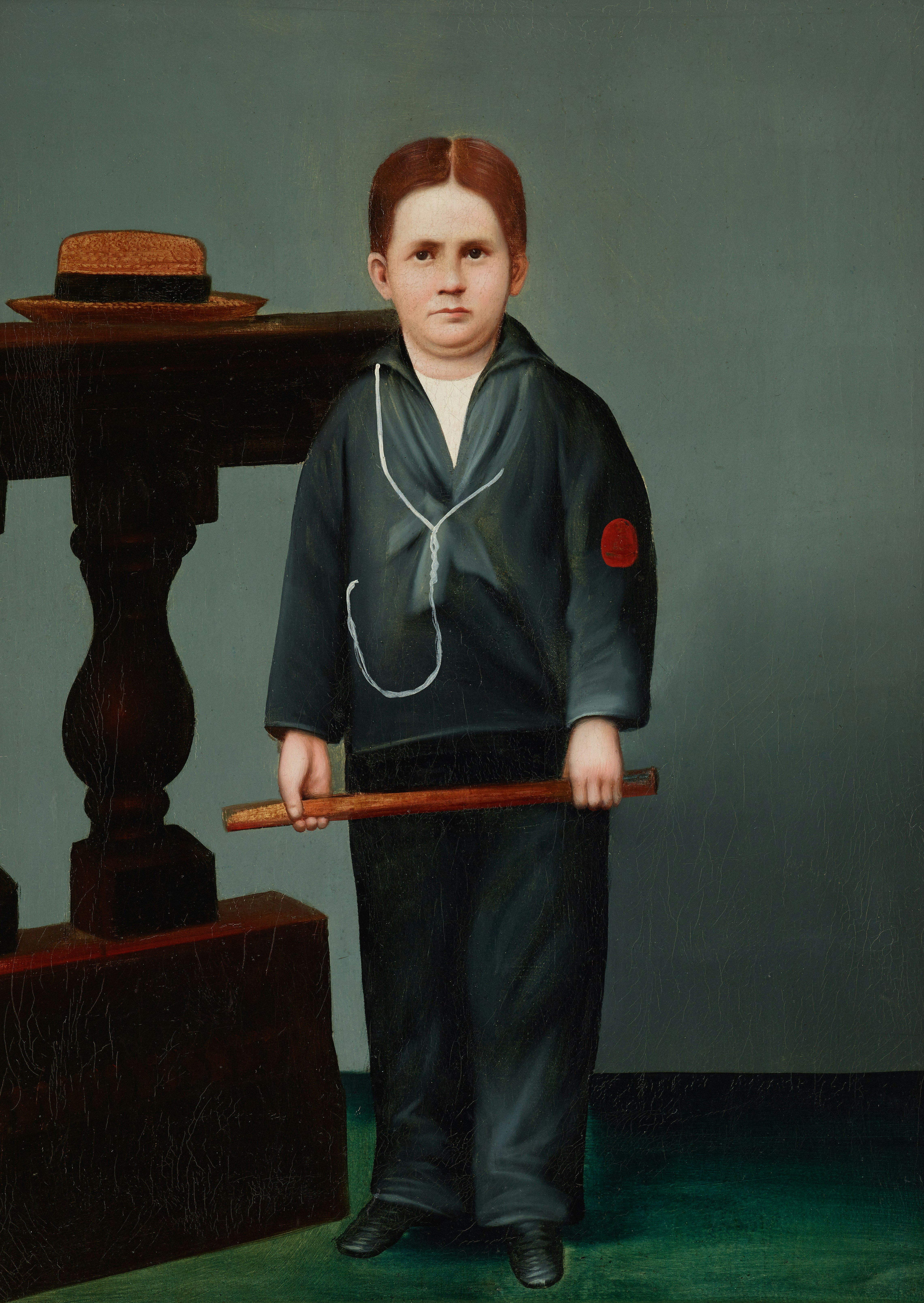 A young boy in a dark suit holds a stick.