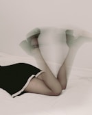 A pair of legs wearing platform heels is raised on a white surface. The image appears to have a motion blur effect, creating a dynamic and artistic feel. The lower portion of the legs is clothed in a dark garment with a decorative white trim.