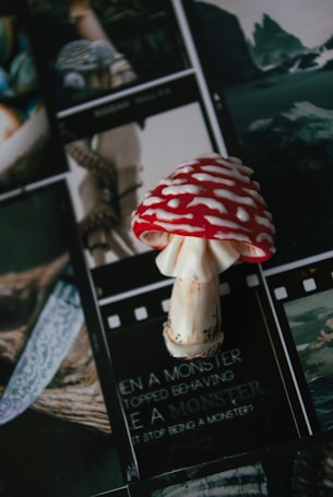 A red and white spotted mushroom sits on top of several film strips that feature various images, including a knife and nature scenes. Text on the film strip below the mushroom is partially legible, referencing a monster.