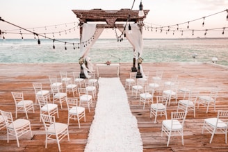 a wooden dock with white chairs and a white aisle