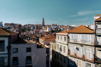 European cityscape featuring tightly packed residential buildings with terracotta rooftops. A tall tower and cranes are visible in the background, indicating urban architecture and development.