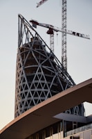 A modern office building under construction with steel framework and cranes.