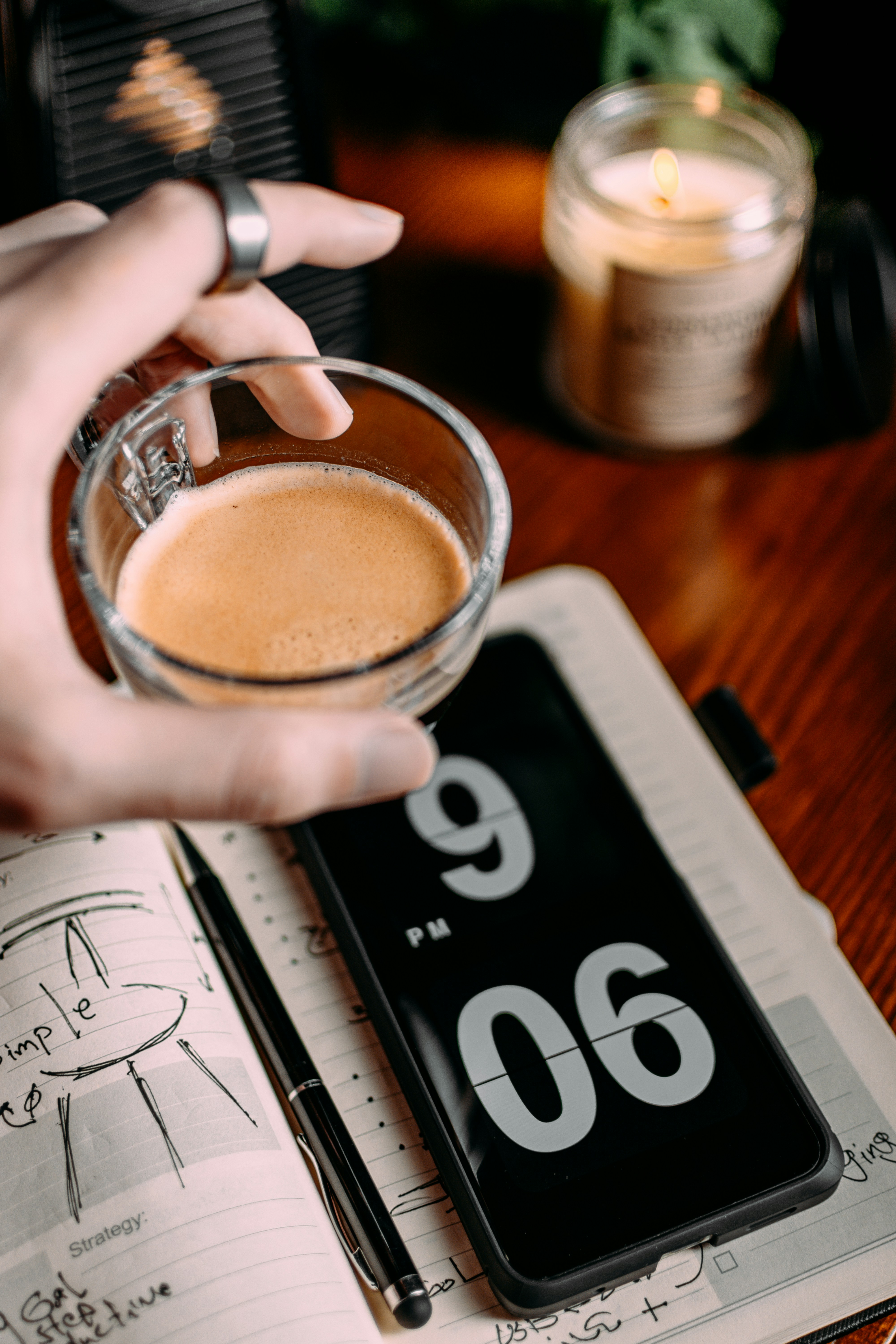 Manos sosteniendo un teléfono con una notificación de recordatorio en pantalla, sobre una mesa con café por la mañana