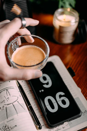 Dimly lit coffee cup resting on a notebook with handwritten event notes beside a softly glowing candle.