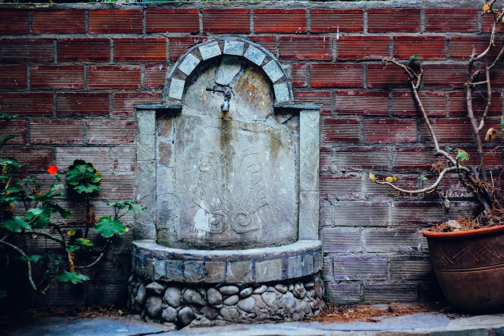 a stone fountain in front of a brick wall