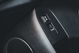 A close-up of a car's interior showing a door panel with a window control switch and door lock buttons. The panel surface is textured with a grainy pattern, and the buttons feature icons for lock and unlock, as well as an auto button for windows.