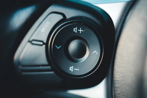 Driver’s hand adjusting volume knob on šarvys head unit, details of brushed metal finish visible.