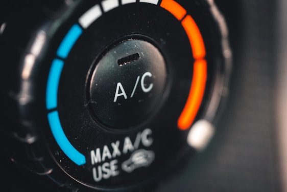 A close-up view of a car's air conditioning control knob, displaying temperature settings. The dial has blue and red colors indicating cooler and warmer temperatures, with the letters 'A/C' in the center. The text 'MAX A/C USE' appears below the dial.