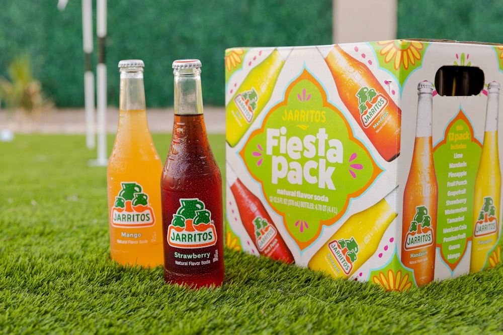 three bottles of soda sitting on top of a lush green field