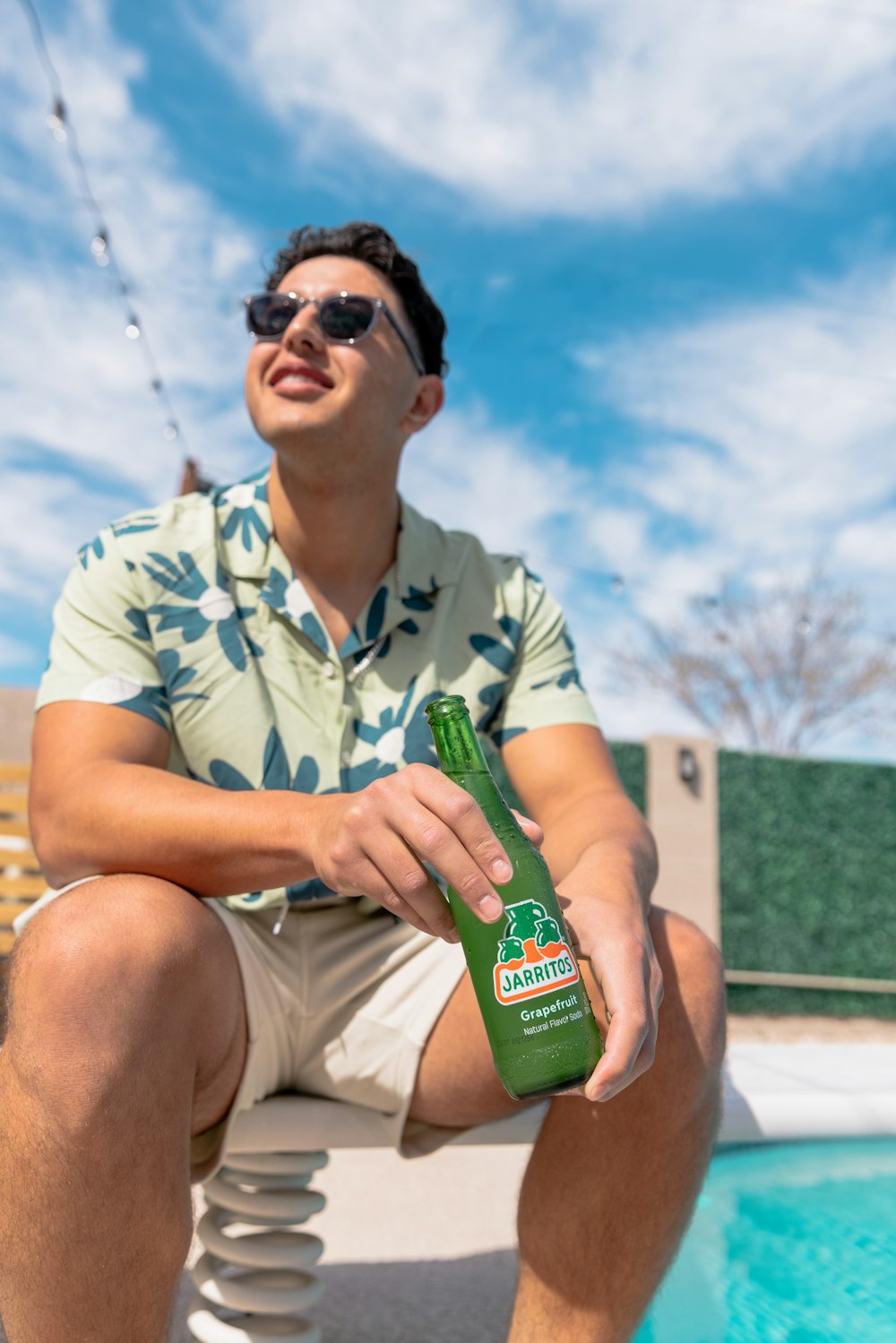 a man sitting next to a pool holding a bottle of beer