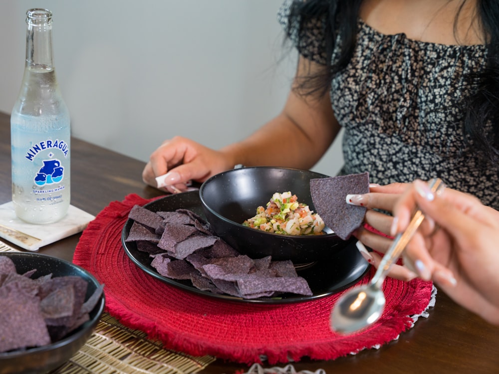 a woman sitting at a table with a bowl of chips and a bottle of water