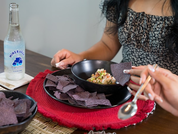 A woman sitting at a table with a bowl of chips and a bottle of water
