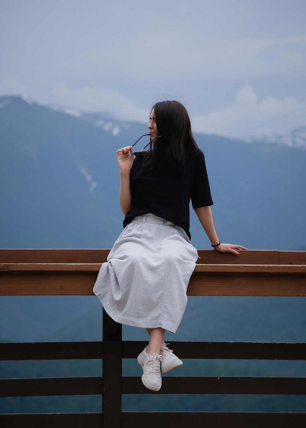 a woman sitting on top of a wooden fence