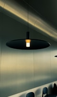 Modern wooden pendant light hanging over a sleek black dining table in a minimalist room.