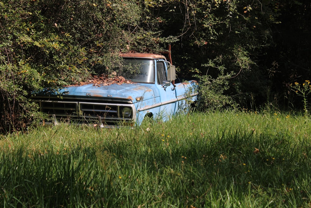 an old blue truck sitting in the middle of a field